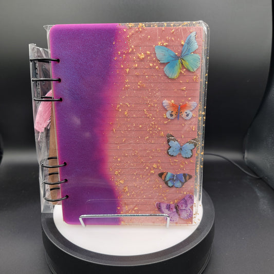 Notebook with butterfly designs on a pink and purple gradient cover, held by a stand.