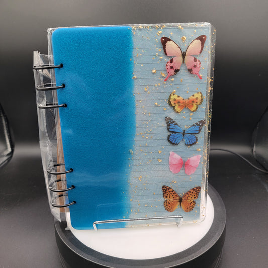 Notebook with butterfly designs on a clear stand against a dark background