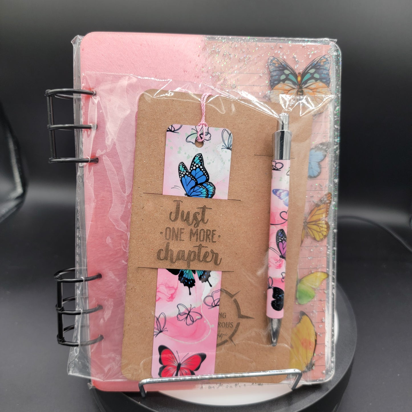 Notebook with butterfly design, pen, and decorative elements on a black surface