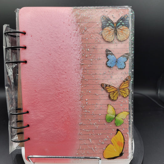Notebook with pink cover and colorful butterflies on a black background