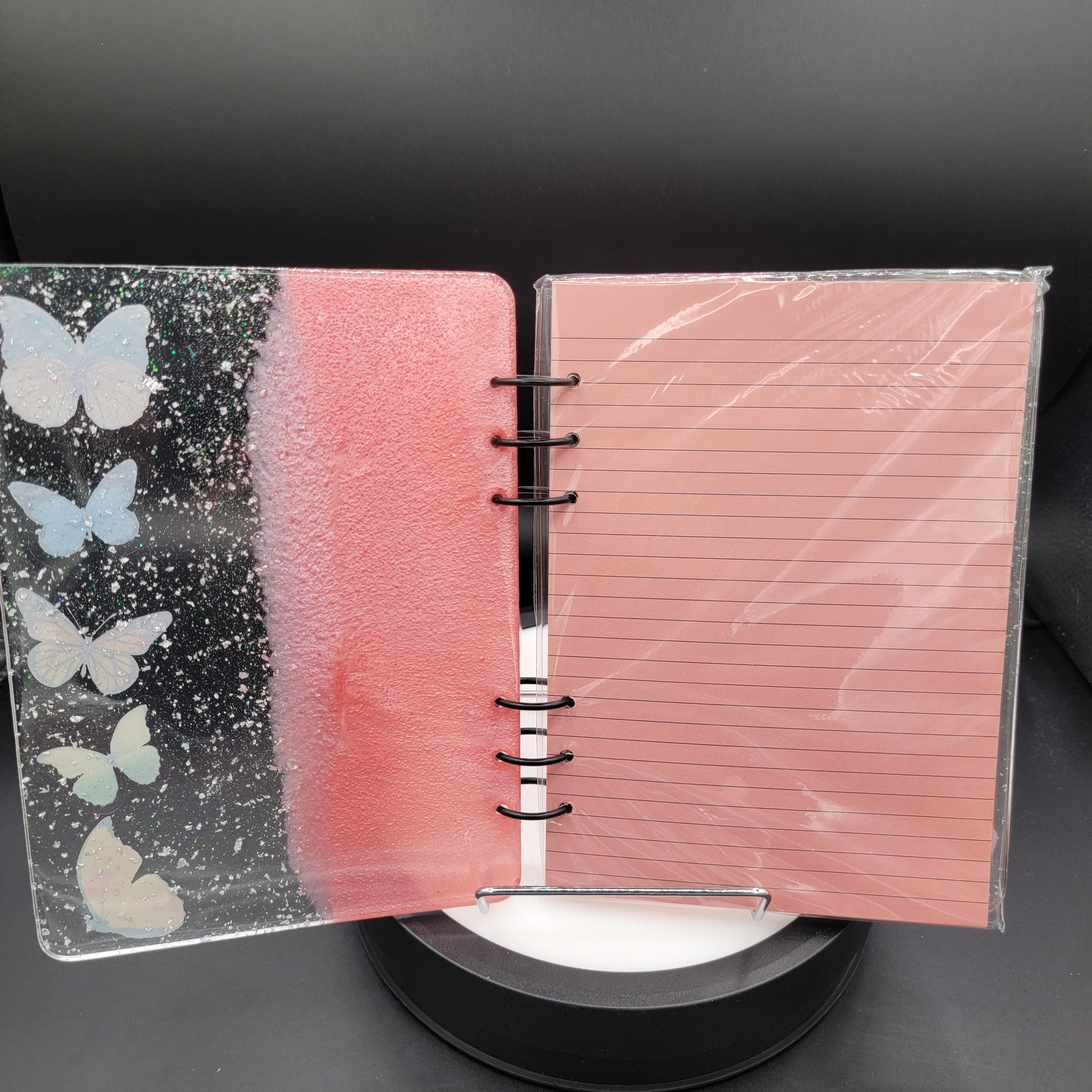 Notebook with a pink cover and black bottom section with butterfly designs on a dark background