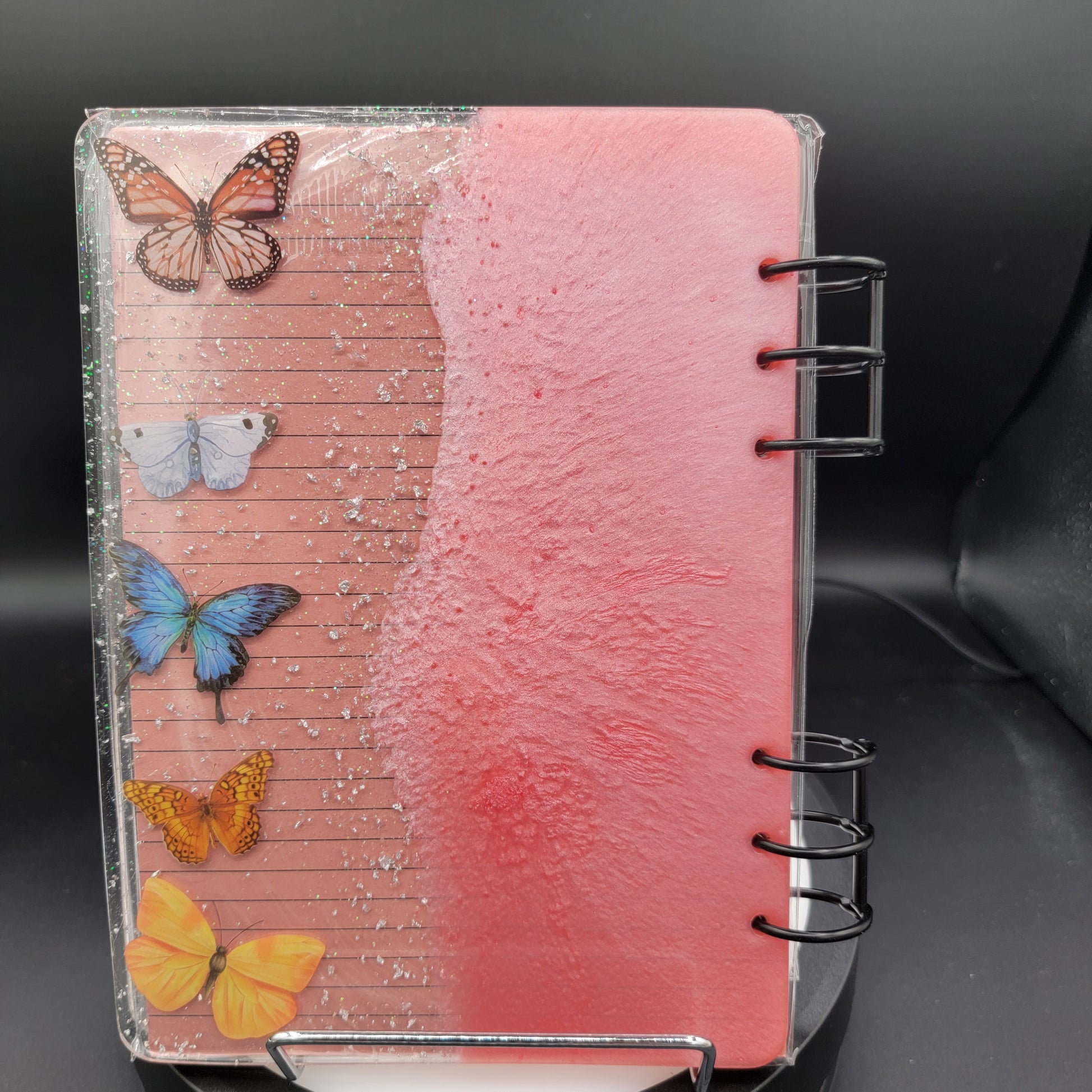 Notebook with butterfly designs on a pink textured cover against a black background