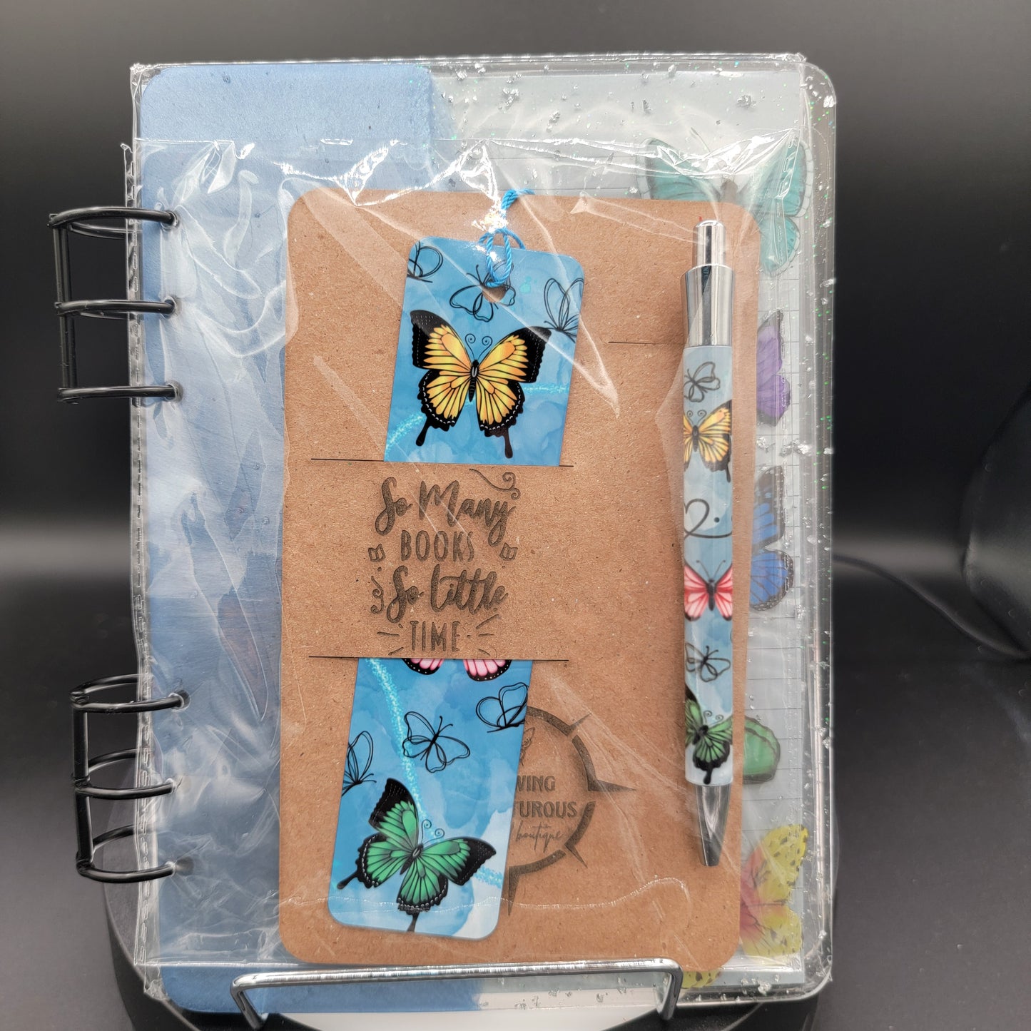Notebook with butterfly designs, a pen, and decorative stickers on a clear cover.