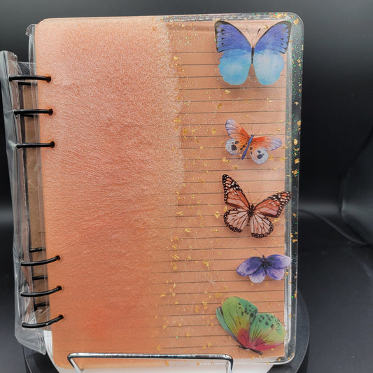 Notebook with butterfly designs on a clear stand against a dark background